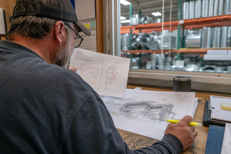 Mechanical detailer comparing a returned shop drawing with red markup against a revised printout
