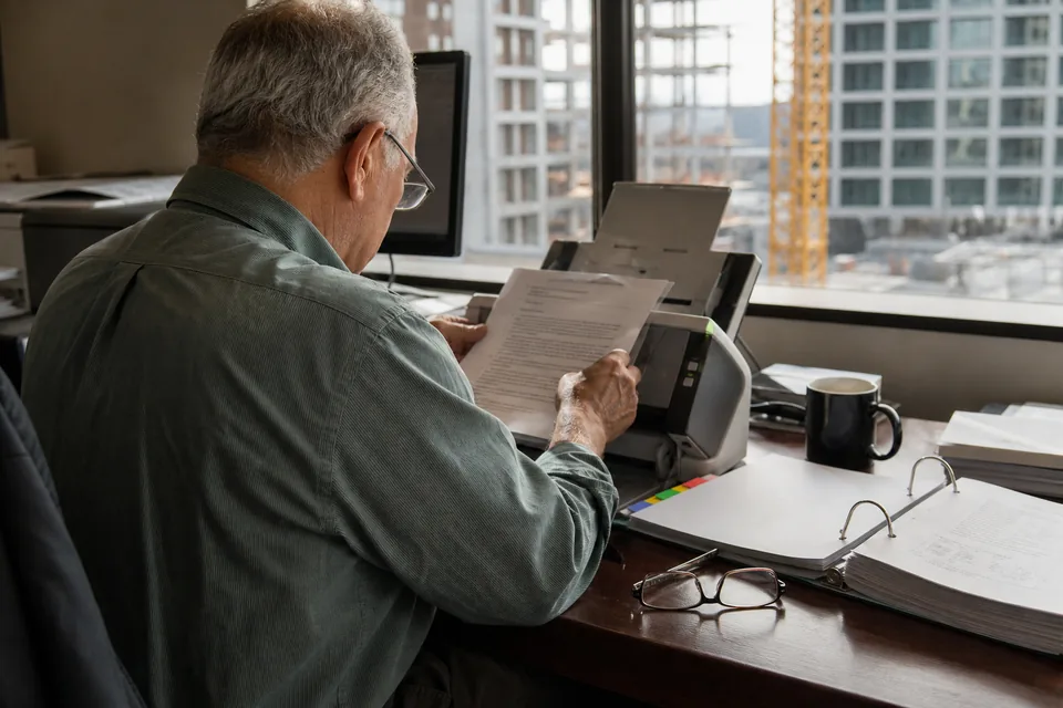 Document controller scanning pages of a printed project manual binder at a general contractor office