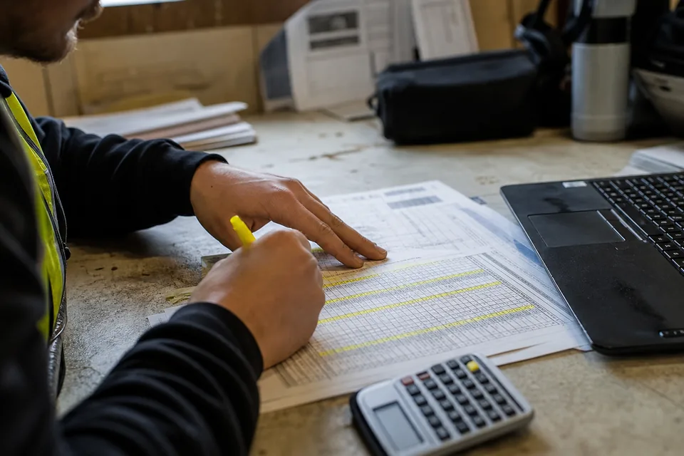 Assistant project manager highlighting rows on a printed spreadsheet submittal log in a site office