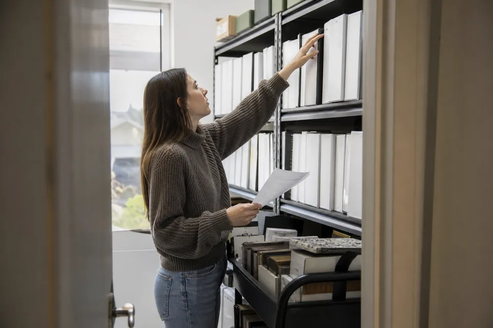 Project coordinator taking a labeled binder from a shelf of submittal binders organized by spec division