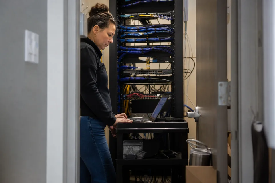 IT lead checking a network rack in a locked server closet at a construction company office