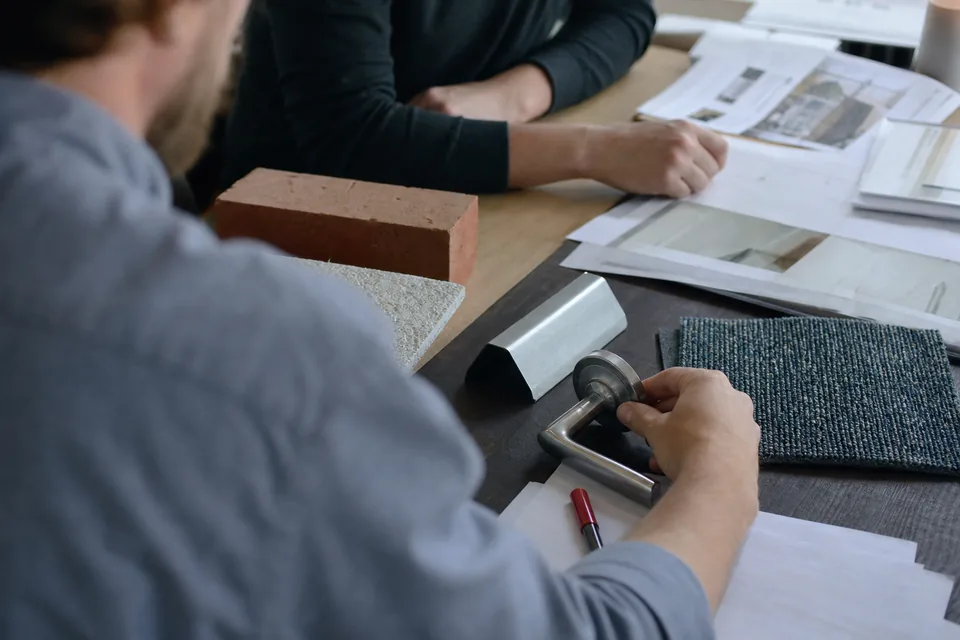 Architect's review table with brick, ceiling tile, metal panel and door lever samples next to printed product data sheets